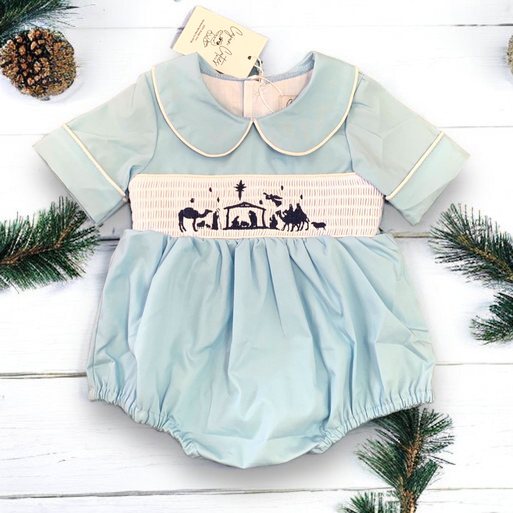 Infant's holiday bubble outfit featuring a smocked nativity scene and a classic Peter Pan collar for an elegant Christmas look."