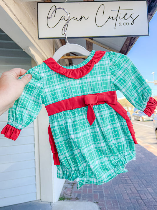 Infant wearing green and white plaid holiday bubble outfit with red bows and a ruffle butt detail.